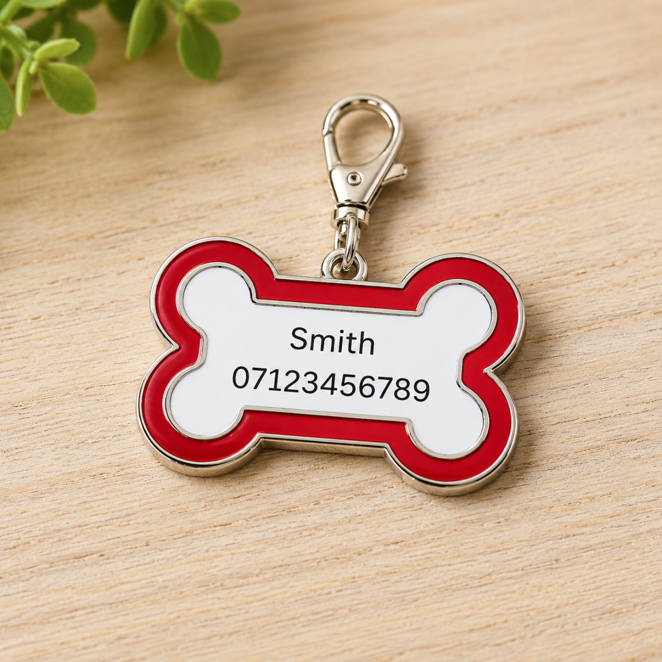 Red and white bone-shaped pet tag with a silver clasp on a wooden surface.
